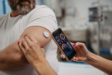 Doctor connecting continuous glucose monitor with smartphone, to check blood sugar level in real...