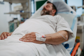 Patient with IV cannula in vein, hand lying in hospital bed. Man in intensive care unit in hospital. IV or intravenous therapy for the overweight man. - obrazy, fototapety, plakaty