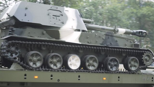 Military tractor transports armored heavy tank on trailer in city. Transportation of military aid for combat operations in war. Export and import of weapons to other countries.