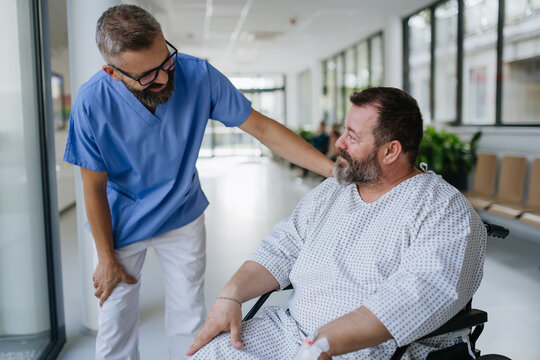 Close up of supportive doctor talking with worried overweight patient in wheelchair. Illnesses and diseases in middle-aged men's health. Compassionate physician supporting stressed patient. Concept of