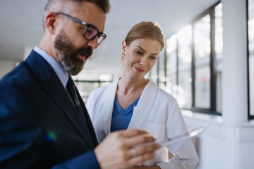 Pharmaceutical sales representative talking with female doctor in medical building. Hospital director consulting with healthcare staff. - obrazy, fototapety, plakaty