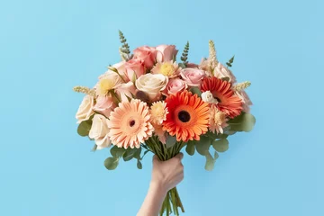  Female hand holds a bouquet of flowers on blue background close-up. © TATIANA KIM