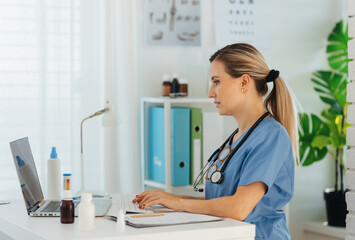 Side view of beautiful female doctor working on laptop in doctor's office. Physician doing...
