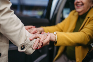 Senior lady getting out of the car, caregiver helping her, holding her hands. Elderly woman has problem with standing up from the car back seat.