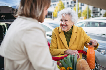 Mature granddaughter helping grandmother load groceries in to the car. Senior woman shopping at the...