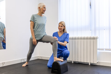 Senior patient at the physiotherapy doing physical exercises with her therapist, doing leg...