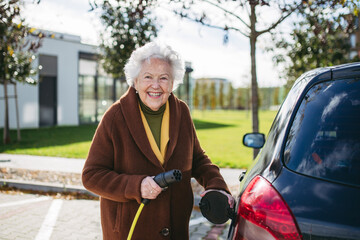 Close up of beautiful senior woman plugging charger in her electric car. Progressive elderly woman...