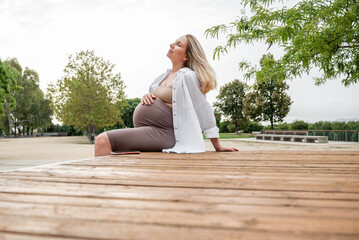 Fototapeta na wymiar Pregnant girl in profile, sitting on a park bench, holding her belly