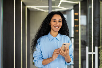 Portrait of a smiling happy businesswoman standing in the office holding a phone in her hands, a...