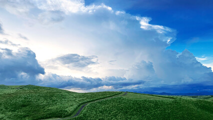 the nature mountain ridge landscape view is a green grass meadow and highland hill mountain road with white cloud cloudy cloudscape on a blue beautiful bright sunny sunlight sky background