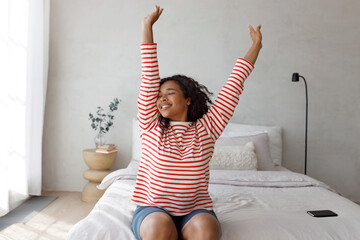 Carefree happy cute african american female with long curly hair posing with raised hands and...