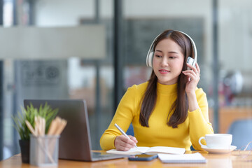 Young asian woman wearing headphones and using a computer laptop listening to music.