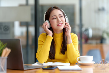 Young asian woman wearing headphones and using a computer laptop listening to music.