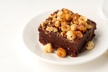 Fototapeta na wymiar Piece of brownie cake with hazelnuts on white background