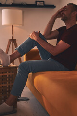 Man with knee pain sitting on a sofa at home.