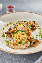 Macro side view of grilled turkey fillet steak, zucchini, and mushrooms, elegantly plated on white ceramic. A grey concrete background adds a minimalist, gourmet touch perfect for a fitness menu