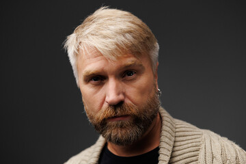 Adult man with blonde hair posing in knitted cardigan isolated on grey 