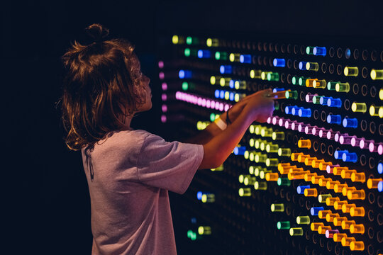 Cute kid boy studying the refraction of light. Child playing with colors flasks in dark room of science museum for children.