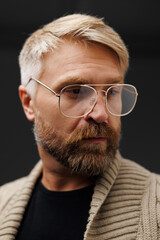 Portrait of confident bearded man in eyeglasses and knitted cardigan isolated on grey 