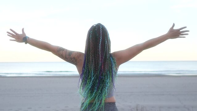 woman with braids breathes and spreads her arms on the beach