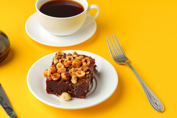 Piece of brownie cake with hazelnuts on yellow background