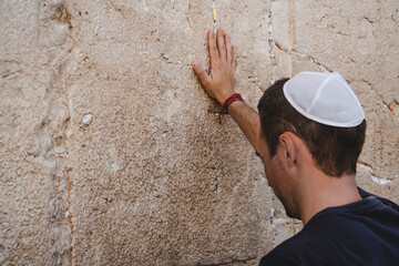 Hand of praying man on the Western Wall in Jerusalem. Tourist in a pile on his head holding the...