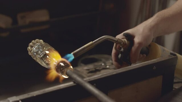 Closeup shot of unrecognizable glassblower in workshop molding shape of elegant glass piece of art with oxy acetylene torch