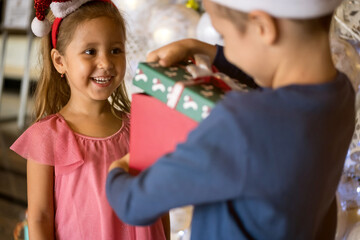 Two adorable little children: brother and sister are exchanging gifts and presents near Christmas tree. Merry Christmas and happy holidays