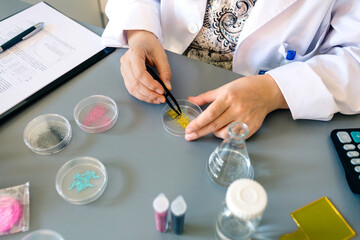 Obraz na płótnie Canvas Unrecognizable female scientist with tweezers examining golden glitter sample over petri dish on environment research laboratory. Woman chemist technician studying dangers of microplastics composition