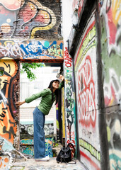 Street Fashion Woman with Green Long Sleeve Shirt,Wide Leg Blue Jeans,Asian femal wearing casual style urban outfits posing near colorful  an open graffiti sprayed wall art during warm summer day