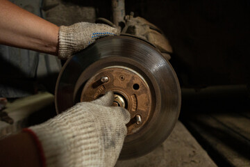 Car repairs. A man unscrews the bolts on a car wheel hub to replace a ball joint. A man wearing...