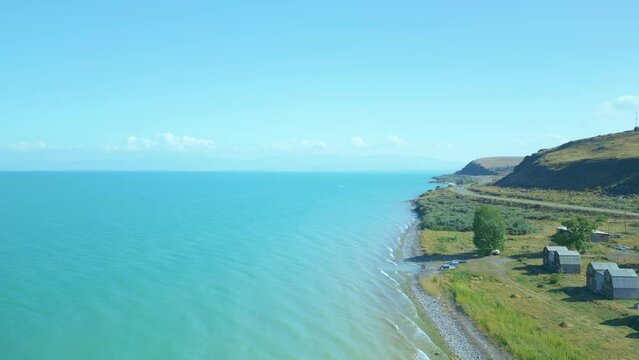 Aerial view of houses and boats, trees, beach big blue azure lake sea in clear sunny weather. Drone video, flying in an arc. Lake Sevan, Armenia.