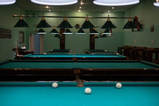 Empty billiard room with green tables illuminated by lamps. Beautiful game room for billiards without people. Many pool tables stand empty, waiting for players.