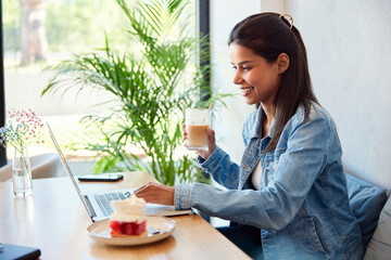 Smiling woman in cafe using laptop drinking coffee