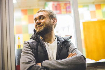 Portrait of a man at a fast food restaurant at night. A man with a beard smiles on a city street at night and waits for his food to be prepared near a cafe. Nightlife concept.