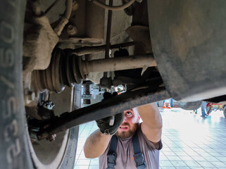 A mechanic unscrews a bolt from the bottom of a car to replace a broken part. A car repair shop...