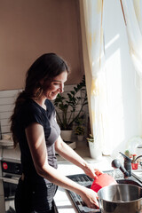 a woman washes dishes in the kitchen by the window