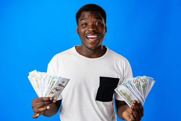Young african man holding cash money in dollar banknotes against blue background