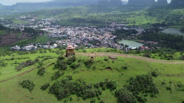 Drone circling around Hindu temple at the edge of the mountain top with the view of Trimbkeshwar town, Ahilya Dam and Trimbak falls in the background surrounded by lush greenery, Nashik, India