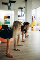 Group of five smiling girls practicing yoga in fitness hall. Young fit women stretching with hands up on mats in gym with big windows and mirror, loft interior.