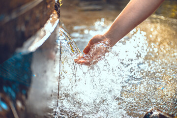 Beautiful photo of a hand under a stream of clear spring water. The woman lowered her hand to touch the stream of clean spring water. The hand touches the cool stream of water.