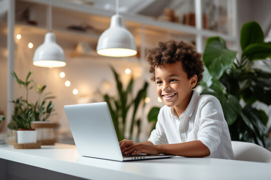 Smiling African American boy sitting at desk with laptop in cozy room. Smart black kid doing his homework, having online lesson, participating in web meeting with tutor. Home schooling concept.