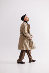 Stylish bearded man in classic outfit and trench coat walking on grey 