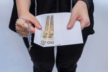 Kobieta trzyma w rękach kopertę z polskimi pieniędzmi i różaniec , datek na kościół 