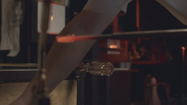 Cropped shot of glassblowing master crafting glass decorative elements by connecting melted pieces of transparent glass together