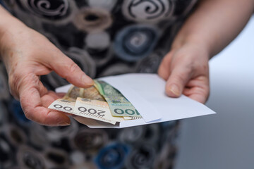 Starsza kobieta wklada pieniądze, polskie banknoty, do koperty