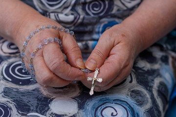Starsza kobieta trzyma dłoniach różaniec z krzyżem i modli się do Boga