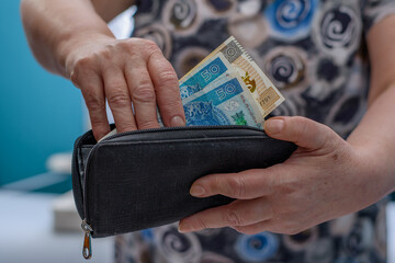 Starsza kobieta płaci pieniądzmi wyjmowanymi z portfela, polskimi banknotami pln