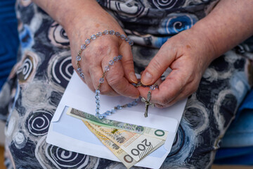 Wizyta duszpasterska księdza po kolędzie, starsza pani trzyma w dłoni różaniec i kopertę z pieniędzmi 