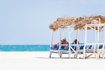 Senior couple relaxing on deck chairs at the beach.White sandy beach and turquoise ocean,luxury beach house.
